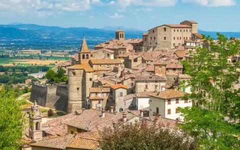 Borgo medievale con tetti in cotto e una torre campanaria, incastonato tra dolci colline verdi. Un luogo che evoca il fascino del **passo dello spino**.