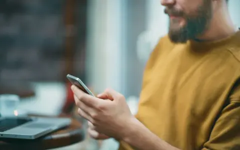 Uomo con barba usa smartphone, forse per capire cosa sono i gb del cellulare e quanto spazio ha per foto e app.