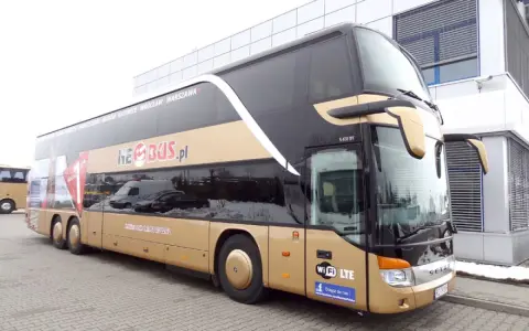 Złoty dwupiętrowy autokar Neobus.pl zaparkowany przed budynkiem.