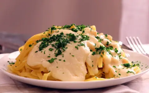 Pasta Alfredo cremosa con perejil picado en un plato blanco.