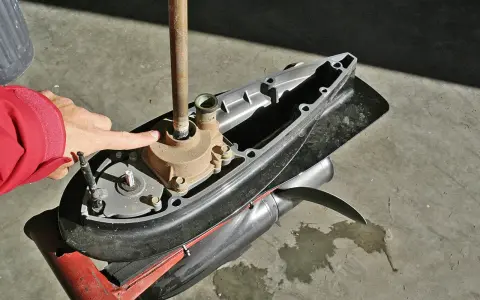 Main d'une personne en veste rouge pointant vers la turbine d'un moteur hors-bord Yamaha 2 temps, prêt à changer la pièce.