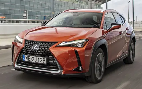 Pomarańczowy Lexus UX 250h w ruchu miejskim, z nowoczesnym grillem i reflektorami LED.