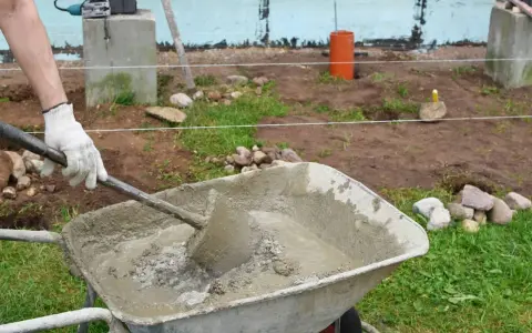 Hombre con guantes mezclando hormigón fresco en carretilla, parte de la puesta en obra del hormigón.