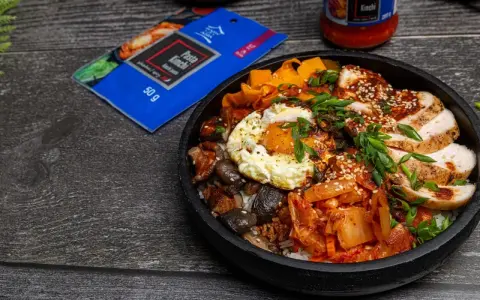 Pyszny Bibimbap przepis: ryż, kurczak, jajko sadzone, grzyby, marchewka i kimchi. Obok opakowanie pasty kimchi.