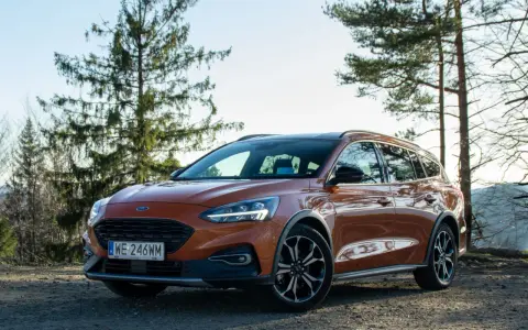 Pomarańczowy Ford Focus kombi na tle drzew i nieba.