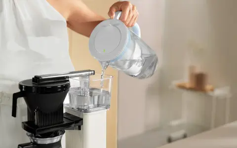 Eine Person füllt Wasser in eine Filterkaffeemaschine, um sie zu entkalken.