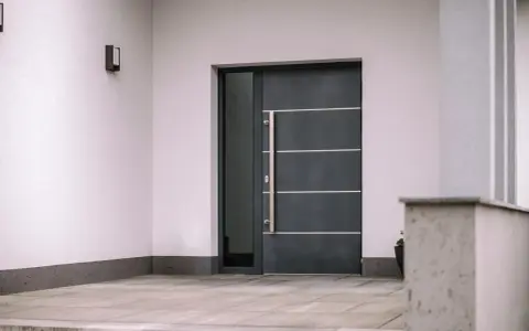 Nowoczesne drzwi wejściowe, ciemnoszare, z długą, metalową klamką i bocznym przeszkleniem. Czy to drzwi stalowe czy aluminiowe?