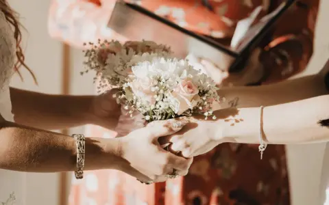 Manos entrelazadas sosteniendo un ramo de flores, un momento íntimo de los rituales boda civil.