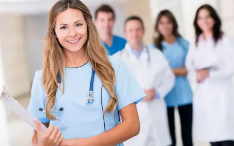 Uśmiechnięta pielęgniarka psychiatryczna z zespołem medycznym w tle. Trzyma tablicę z dokumentami.