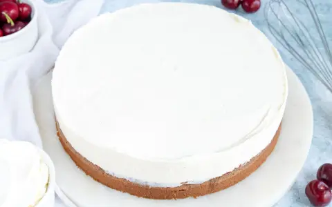 Ein köstlicher Kuchen mit Mascarpone-Creme, garniert mit frischen Kirschen und einem Schneebesen daneben.