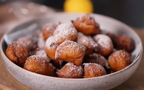 Un bol rempli de beignets dorés, saupoudrés de sucre glace. Parfait pour une recette beignet moelleux rapide.