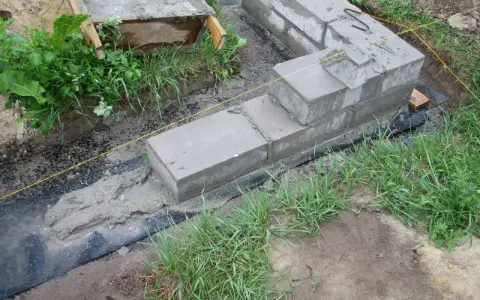 Fundamenty z betonu i bloczków, częściowo zalane, otoczone trawą. Pytanie, czy można zostawić odkryte fundamenty na zimę, jest tu kluczowe.