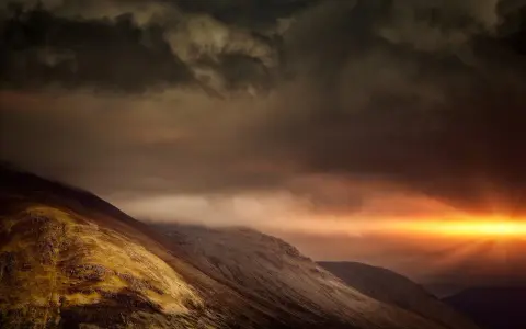 Dramatic sunburst pierces dark clouds over a rugged mountain range, a powerful display of the sovereignty of God.