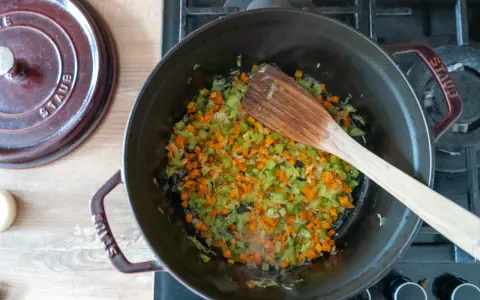 Würziges Sofrito Rezept: Karotten, Sellerie und Zwiebeln werden in einem gusseisernen Topf angedünstet.