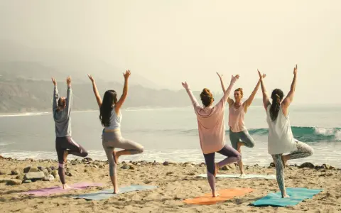 Kvinnor i trädposition på stranden. En lugn morgon för yoga, kanske en paus från pilates.