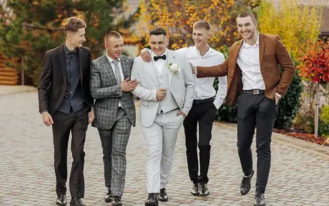 Pięciu mężczyzn w garniturach, idealnych na wesele w upał. Jasny garnitur pana młodego i eleganckie stylizacje drużbów.