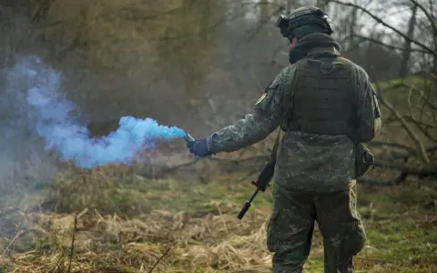 Żołnierz w kamuflażu odpala niebieski granat dymny, przestrzegając zasad ASG.