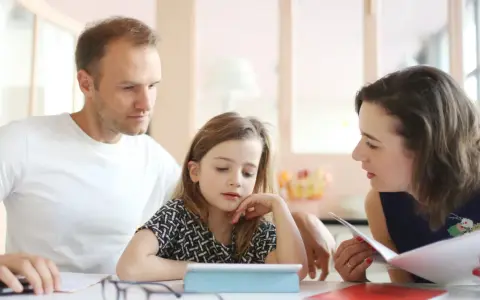 Rodzice pomagają córce w nauce, omawiając przykłady równoważników zdań.