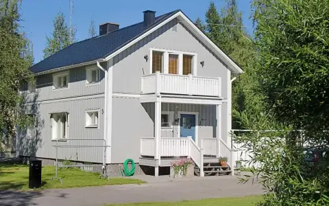 Maison à deux étages avec une peinture suédoise blanche, un balcon, une porte bleue et un jardin verdoyant.