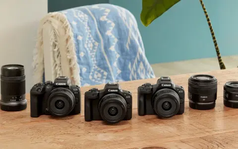 Trzy czarne aparaty Canon EOS z obiektywami i dodatkowe obiektywy na drewnianym stole.