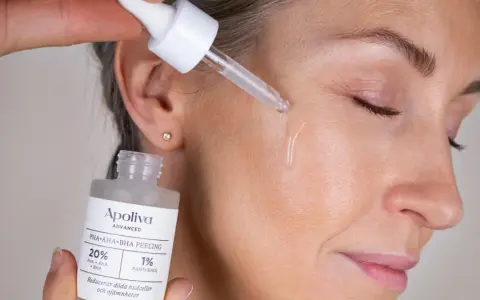 Droppe av aha-syra ansikte-serum appliceras på huden. En flaska med peeling syns i förgrunden.