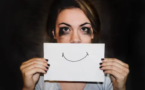 Dziewczyna z rozmazanym makijażem ukrywa usta za kartką z uśmiechem. Trudna samoregulacja emocji.
