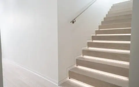 Scala moderna con gradini in legno illuminati e un discreto profilo battiscopa filo muro che ne esalta la pulizia delle linee.
