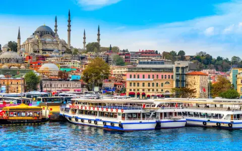 A vibrant cityscape of Istanbul, with the Suleymaniye Mosque dominating the skyline. Ferries and buses line the waterfront, ready for a 3-day Istanbul adventure.