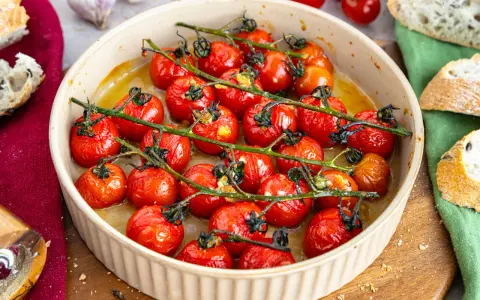 Konfierte Tomaten in einer Auflaufform, mit Brot und Knoblauch daneben.
