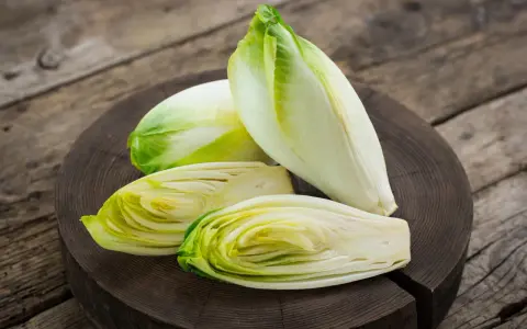Frische Chicorée-Köpfe, einer davon halbiert, liegen auf einem Holzbrett. Perfekt für einen knackigen Chicorée-Salat.