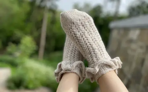 Piernas con calcetines de crochet color crema, con volantes en los tobillos y un delicado patrón calado.