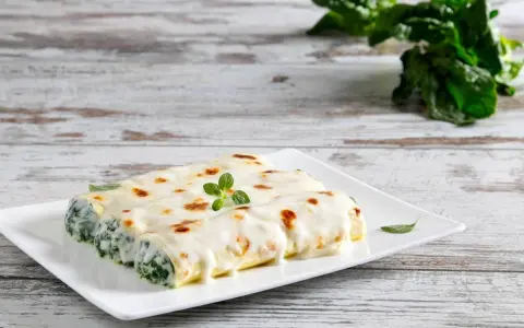 Cannelloni ricotta e spinaci fumanti, ricoperti di besciamella e gratinati, guarniti con un rametto di origano.