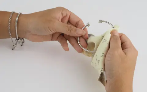 Manos puliendo un brazalete de plata con un paño. Aprende cómo limpiar la plata para que brille como nuevo.