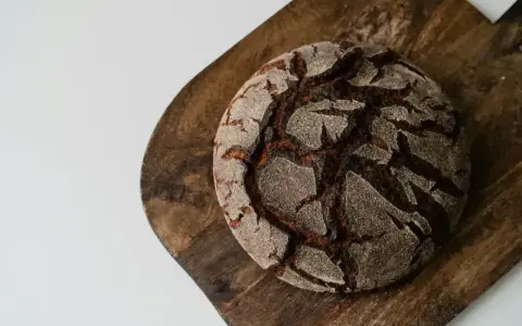 Chleb bez mąki, ciemny, okrągły bochenek z popękaną skórką, leży na drewnianej desce.