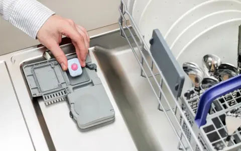 Dłoń wkłada tabletkę do zmywarki. Może to być rozwiązanie problemu, gdy zmywarka nie domywa górnego kosza.