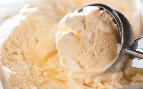 Ein Löffel nimmt eine Kugel cremiges Eis auf. Kleine eiskristalle im eis glitzern im Licht.