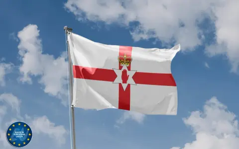 Flaga Irlandii Północnej powiewa na tle błękitnego nieba z chmurami. Symbolizuje historię i tożsamość regionu.