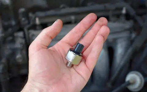 A hand holds a new oil pressure sensor, a potential fix for a p0332 code Chevy Silverado.