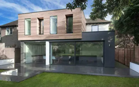 Une extension moderne en bois et anthracite pour agrandir une maison, avec de grandes baies vitrées donnant sur un jardin.