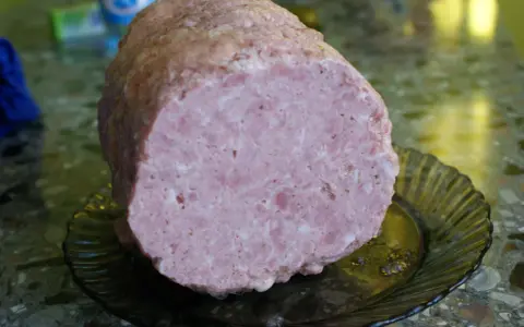 Pokrojona mielonka z szynkowara, różowa i soczysta, leży na ciemnej, karbowanej paterze.