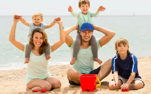 Famiglia felice in spiaggia, un modo perfetto per imparare come abbronzarsi in sicurezza mentre i bambini giocano con secchiello e palette.