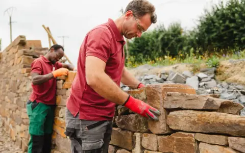 Deux maçons construisent un mur en pierre sèche.