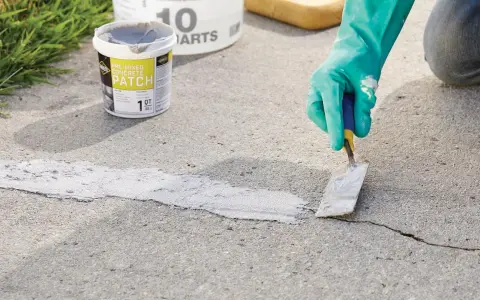 Applying pre-mixed concrete patch to fix cracks in pavement. A gloved hand uses a trowel to smooth the patch.