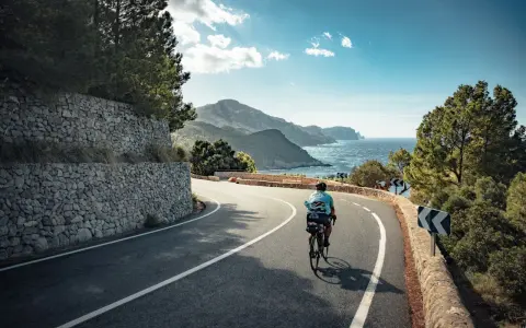 Rennradfahrer auf einer kurvigen Straße mit Blick auf das Meer und die Berge auf Mallorca.