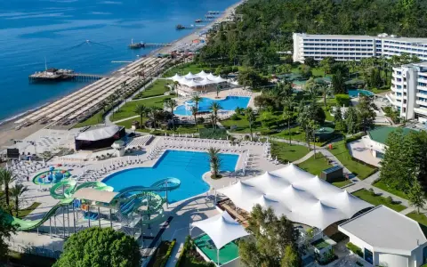 Widok z lotu ptaka na Mirage Park Resort: plaża, baseny, zjeżdżalnie wodne, białe pawilony i hotele otoczone zielenią.