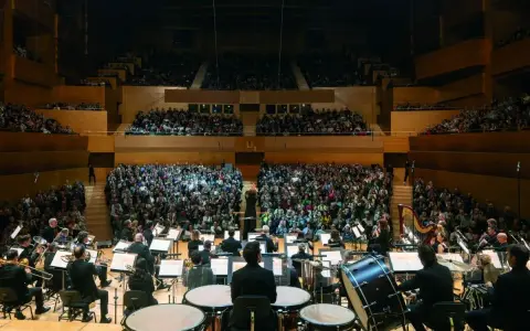 Orquesta sinfónica tocando para un público numeroso. Un director dirige la orquesta, creando una atmósfera mágica para los conciertos infantiles.