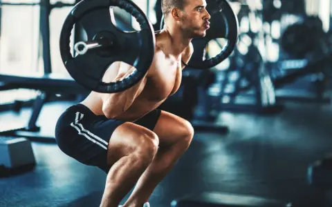 Man gör ett tungt benspark hemma med skivstång på axlarna i ett gym.