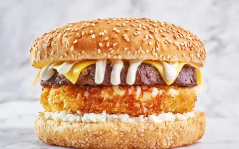 Pyszny burger drwala przepis: soczysty kotlet, chrupiące panierowane jajko, ser i biały sos na sezamowej bułce.