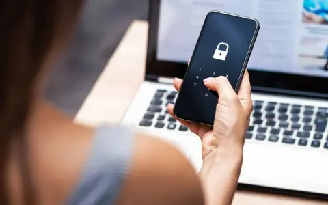 Frau entsperrt Handy mit Schloss-Symbol, besorgt wegen gehackter mailadresse. Laptop im Hintergrund.
