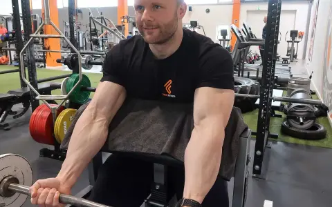 Mann trainiert Bizeps mit Langhantel im Fitnessstudio. Deutlich sichtbare Muskeln beim Bizeps dehnen.